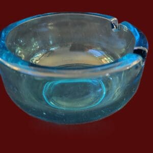 A clear glass ashtray with a round shape on a dark red background.