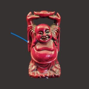 Red laughing Buddha statue with raised arms on black background.