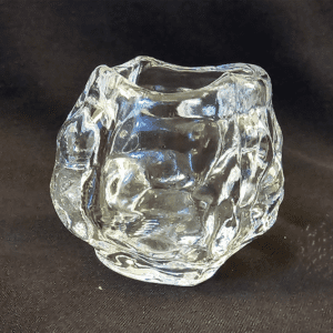 A clear, textured glass vase with an irregular shape on a black surface.