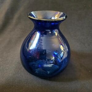 A small blue glass vase with a wide rim on a dark surface.