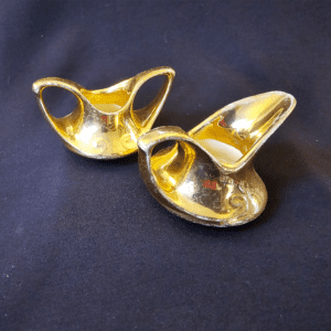 Pair of shiny golden decorative shoe-shaped objects on dark fabric.