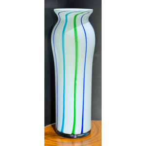 Tall white vase with colorful vertical stripes on a wooden surface.
