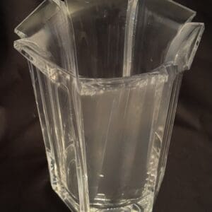 Clear hexagonal glass vase with water on a dark surface.