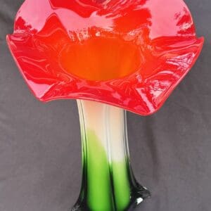 A vibrant red flower-shaped glass vase with green stem-like base.