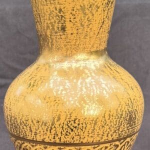 A close-up of a textured, yellowish ceramic vase with a narrow neck and rounded body.