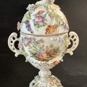 Ornate porcelain egg-shaped container with floral design and handles.
