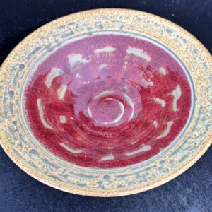 Ornate ceramic plate with red center and intricate rim design.