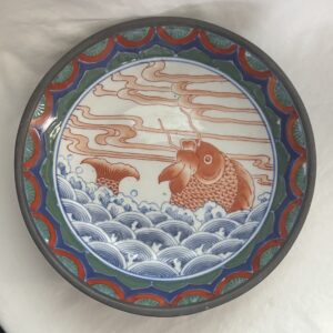 Decorative plate featuring a fish amid waves and clouds.