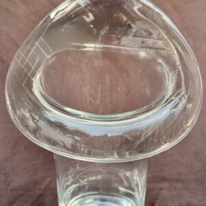 A clear glass mushroom-shaped object on a wooden surface.